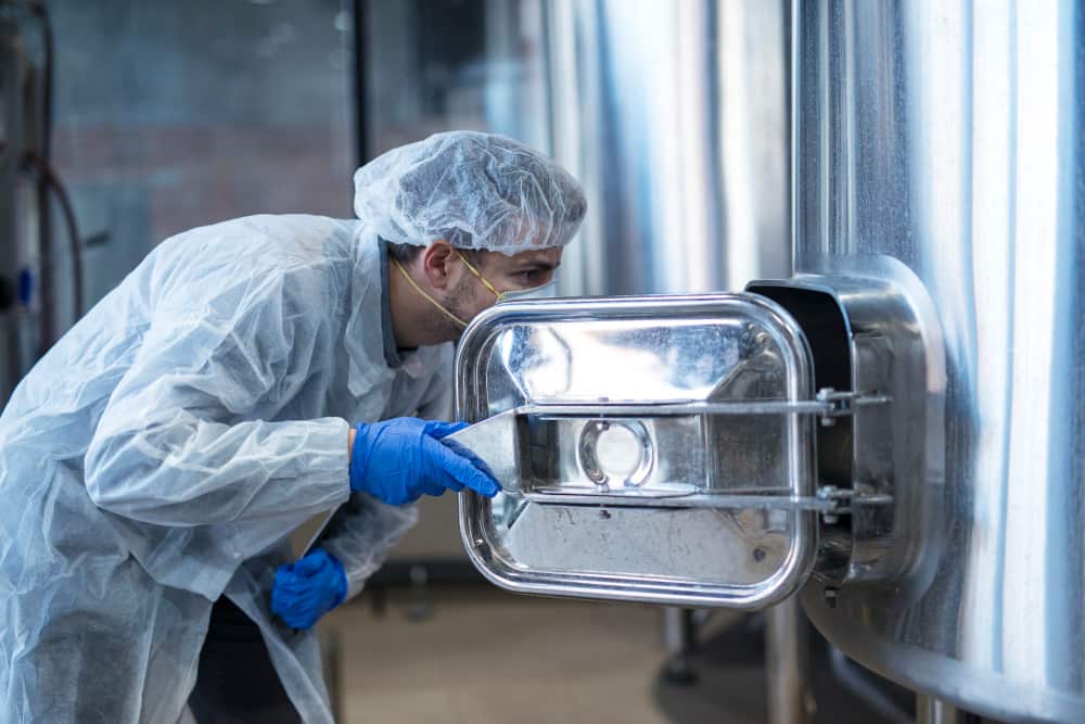 Un technicien en combinaison de protection inspectant l'intérieur d'une cuve industrielle lors d'un entretien du réservoir inox.