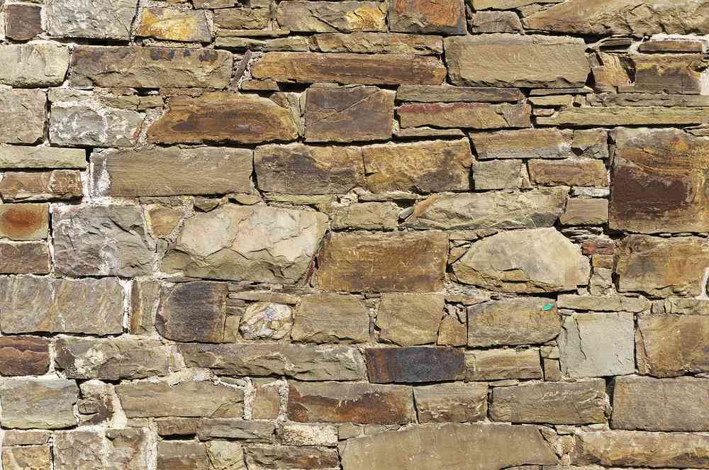 Mur construit avec des pierres de différentes tailles et couleurs, sans mortier apparent