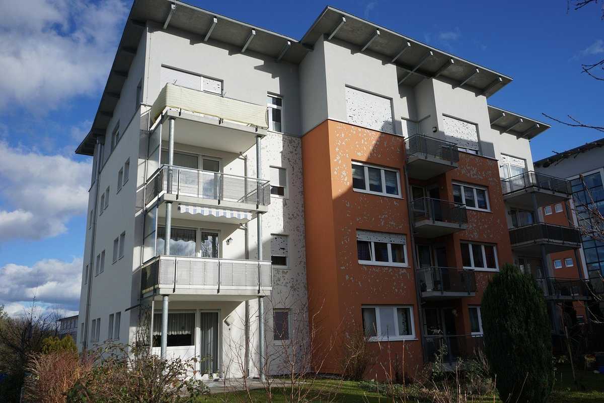 Immeuble blanc et orange à trois étages avec balcons et végétation sous un ciel bleu Immeuble blanc et orange à trois étages avec balcons et végétation sous un ciel bleu